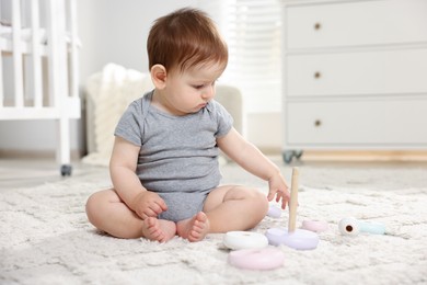 Photo of Cute little baby playing with toy pyramid in room