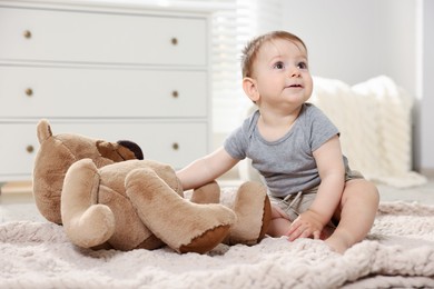 Photo of Cute little baby playing with teddy bear in room
