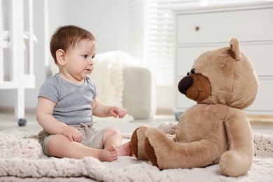 Photo of Cute little baby playing with teddy bear in room
