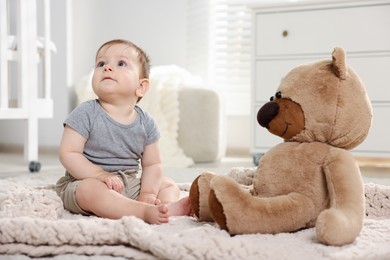 Photo of Cute little baby playing with teddy bear in room