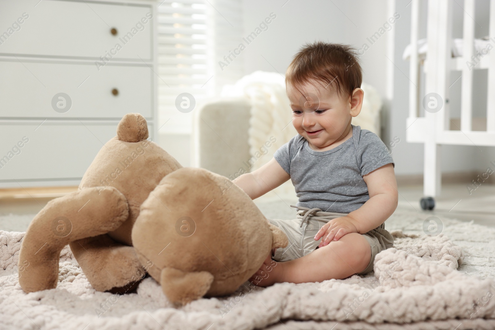 Photo of Cute little baby playing with teddy bear in room