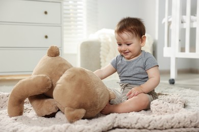 Photo of Cute little baby playing with teddy bear in room