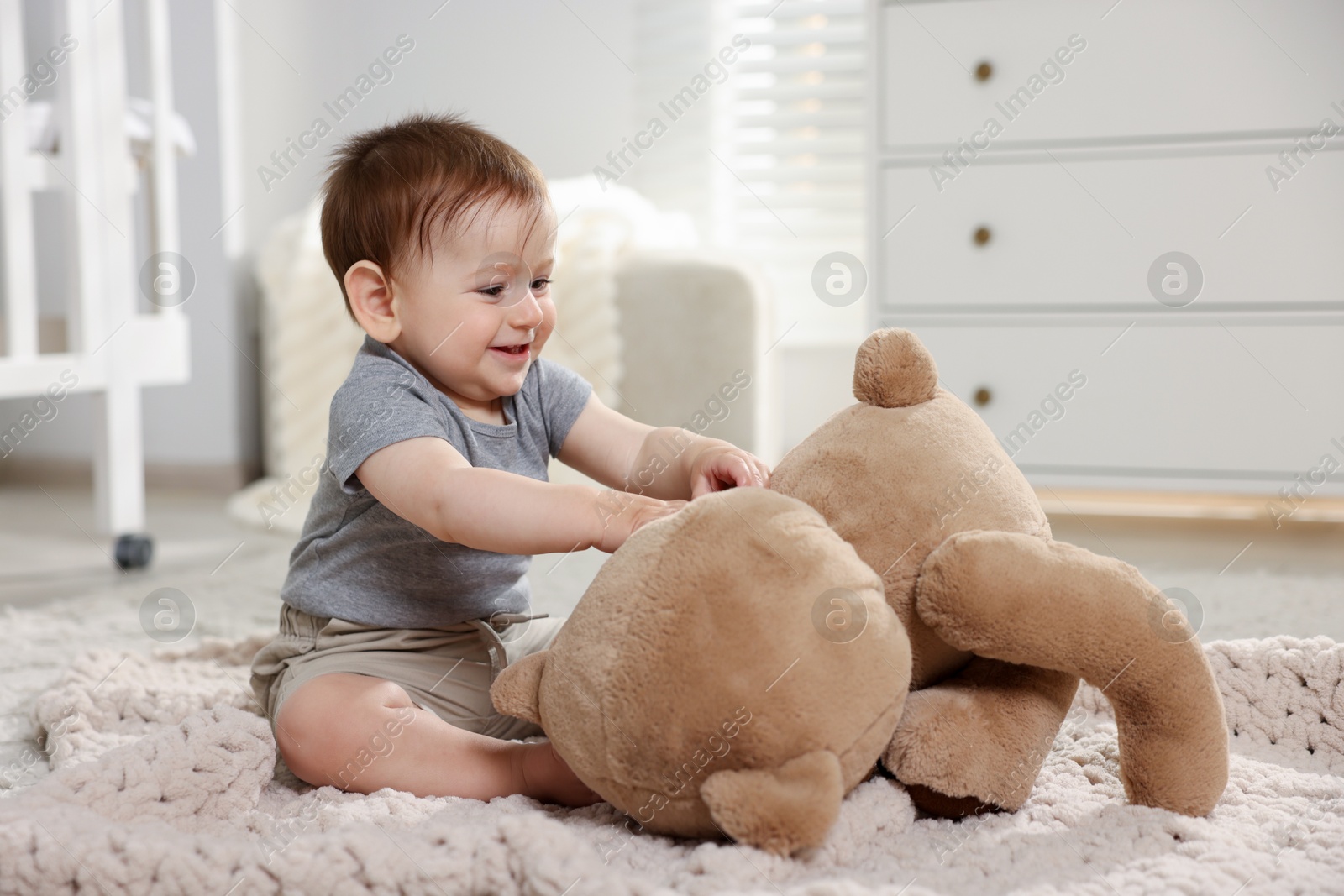 Photo of Cute little baby playing with teddy bear in room