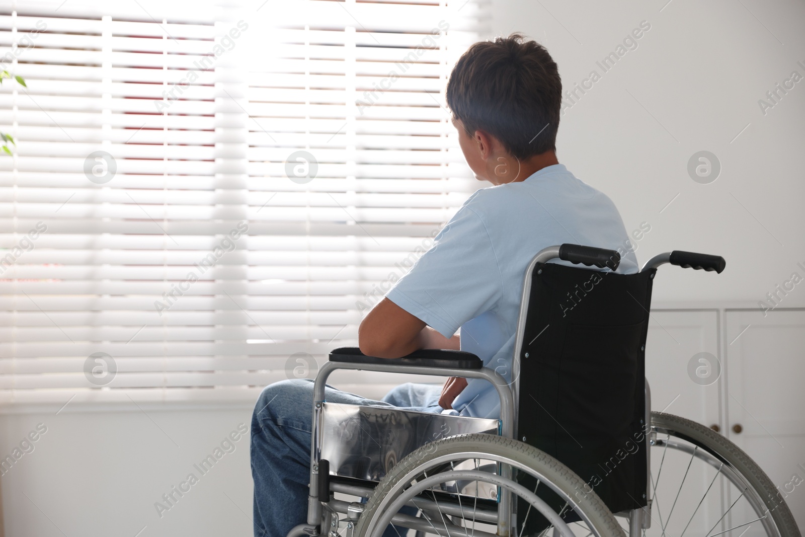 Photo of Teenage boy in modern wheelchair indoors, back view. Space for text