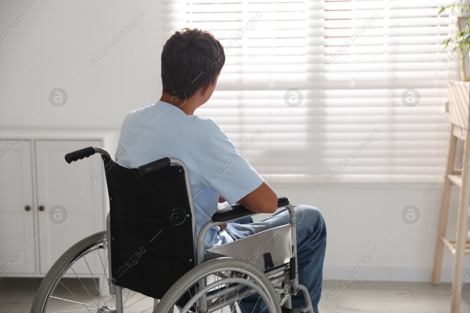 Photo of Teenage boy in modern wheelchair indoors, back view. Space for text