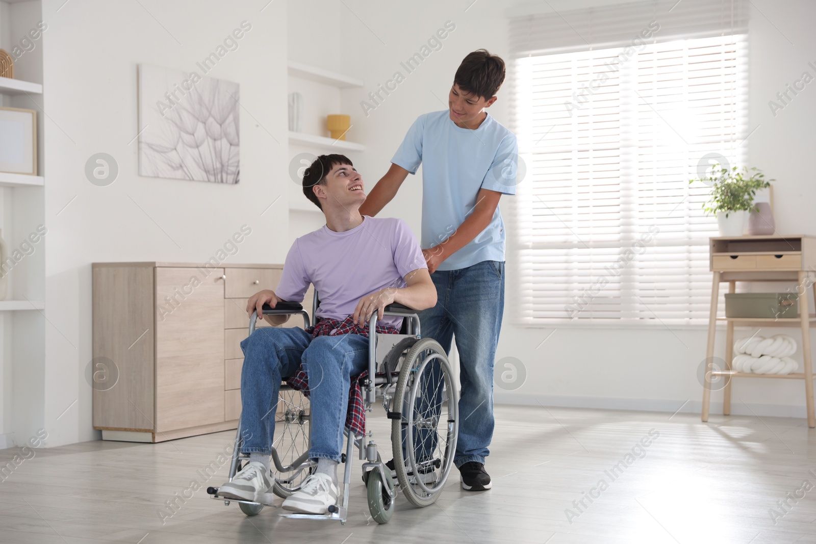 Photo of Happy young man in wheelchair and caregiver indoors