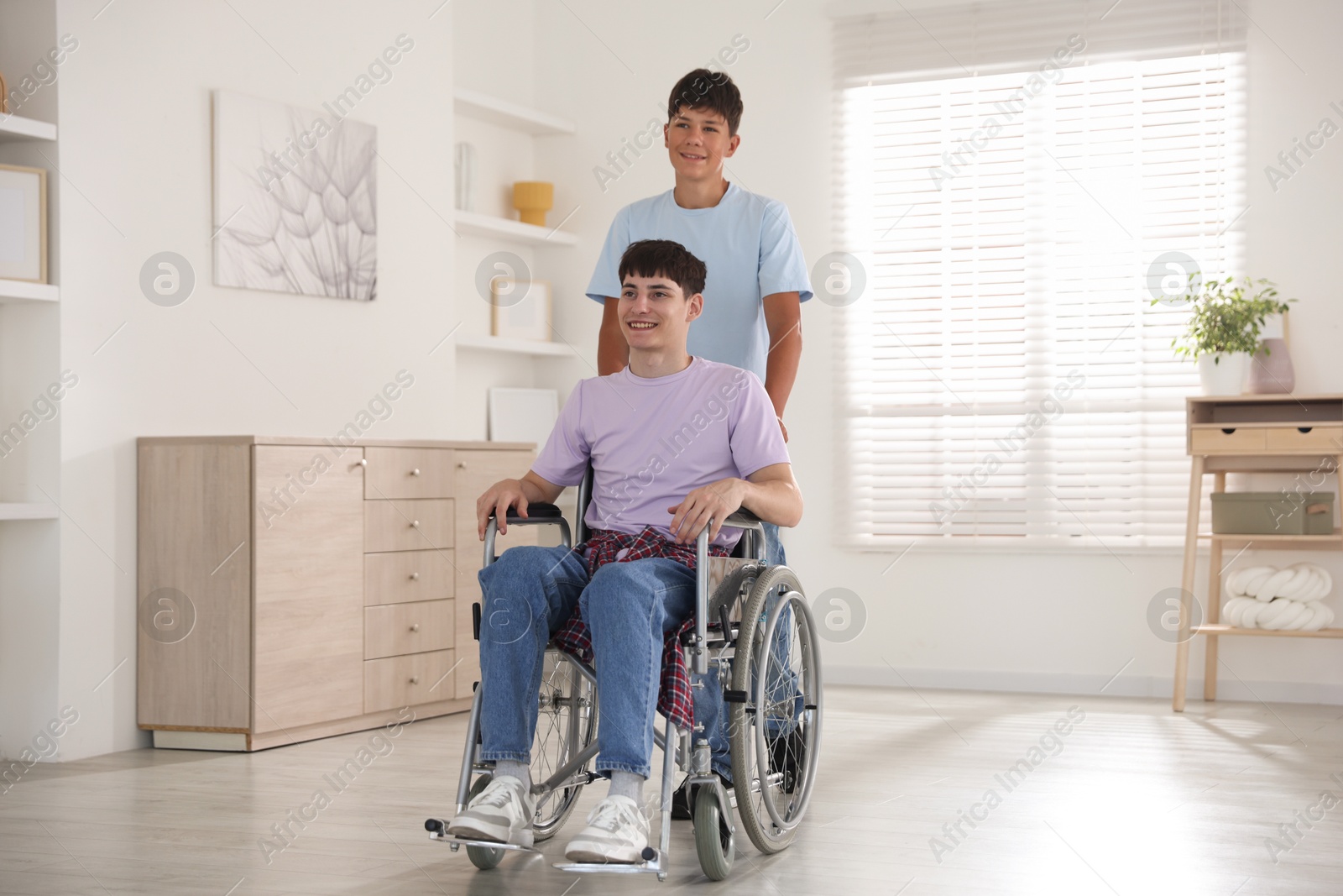 Photo of Happy young man in wheelchair and caregiver indoors
