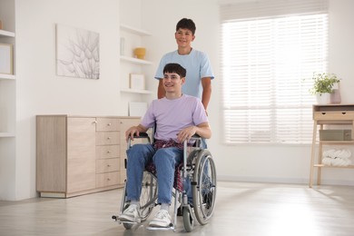Photo of Happy young man in wheelchair and caregiver indoors