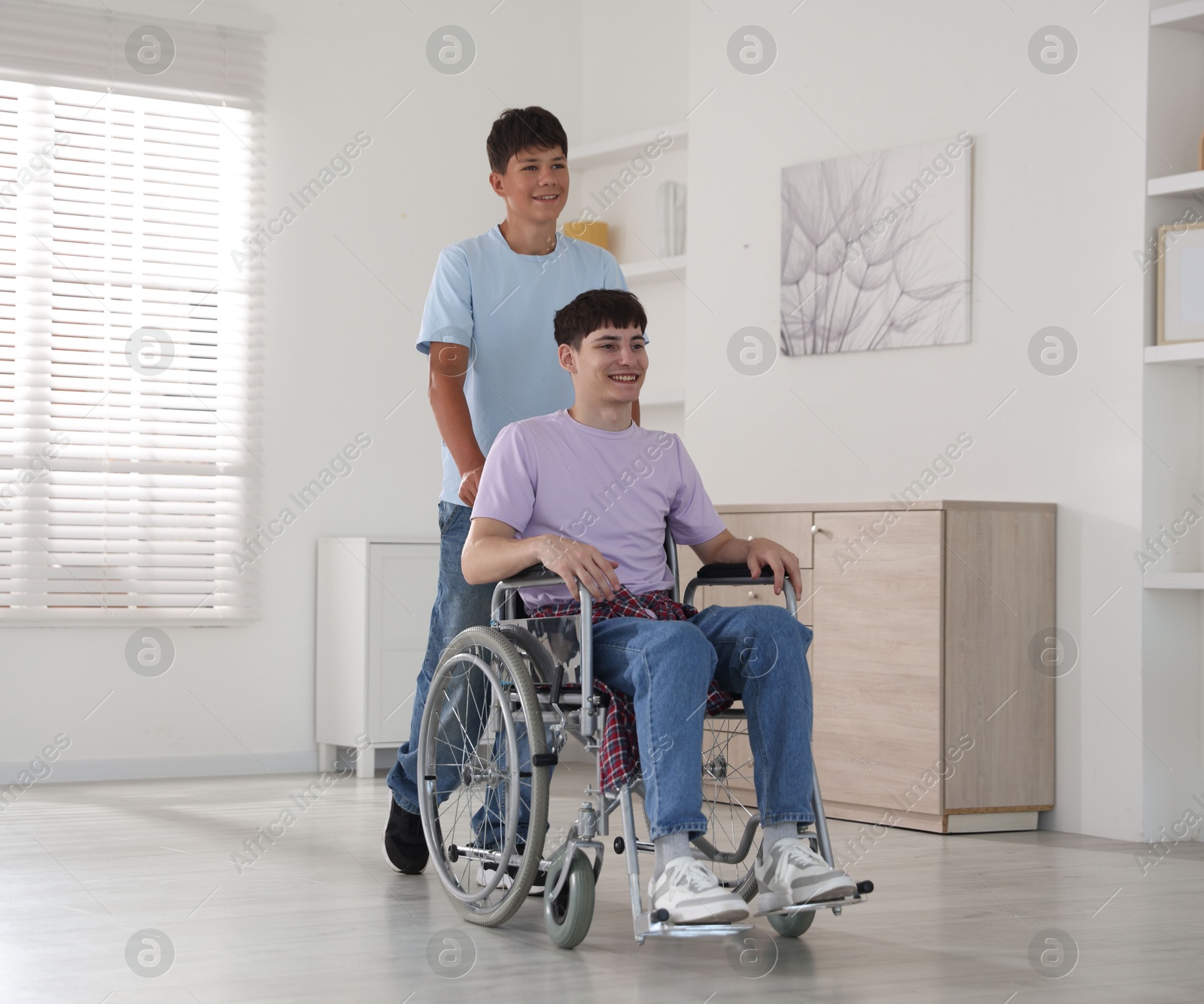 Photo of Happy young man in wheelchair and caregiver indoors