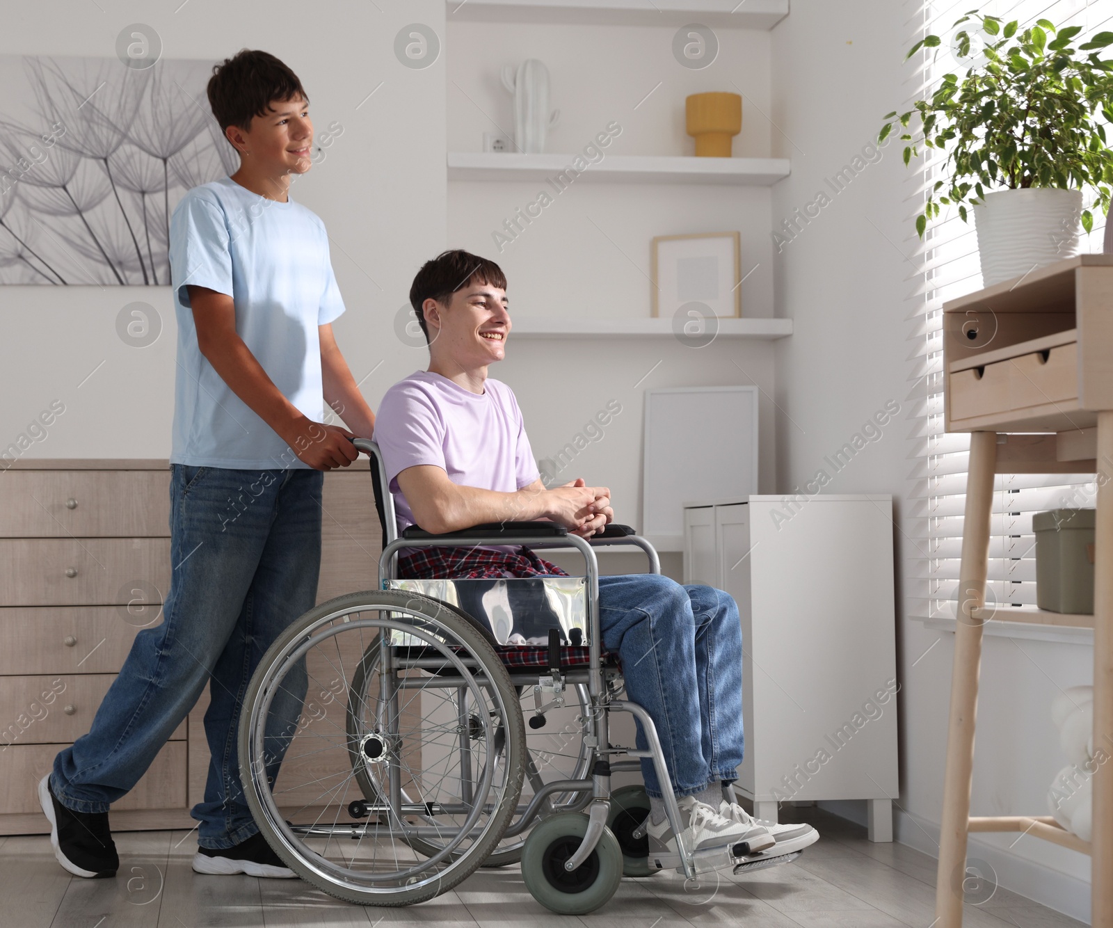 Photo of Happy young man in wheelchair and caregiver indoors