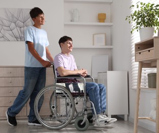Photo of Happy young man in wheelchair and caregiver indoors