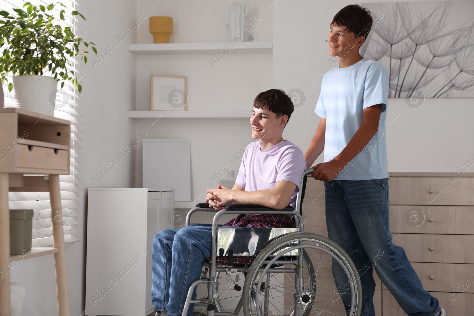 Photo of Happy young man in wheelchair and caregiver indoors