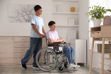 Photo of Happy young man in wheelchair and caregiver indoors