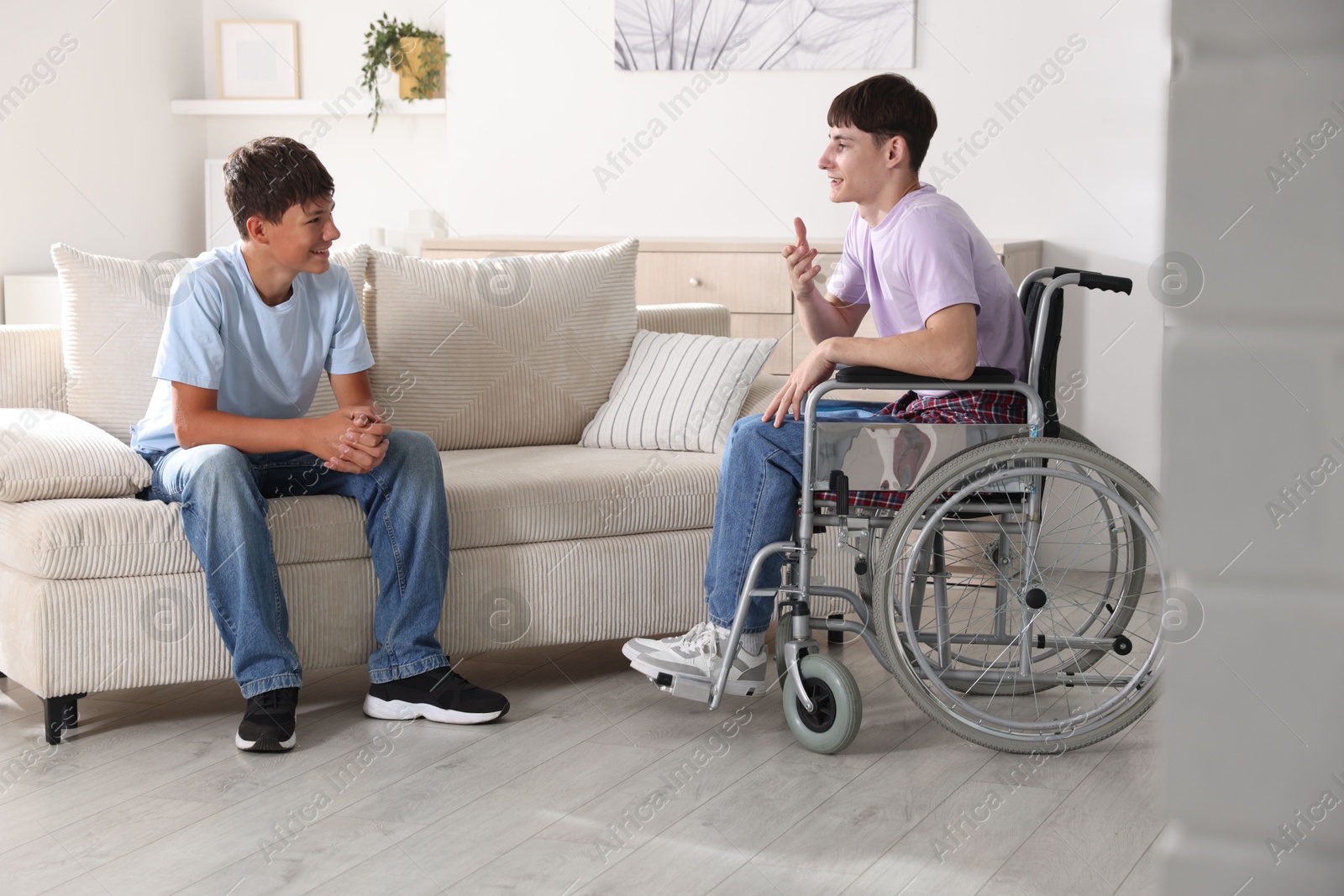 Photo of Happy young man in wheelchair and caregiver indoors