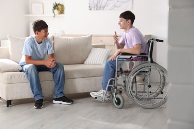 Photo of Happy young man in wheelchair and caregiver indoors