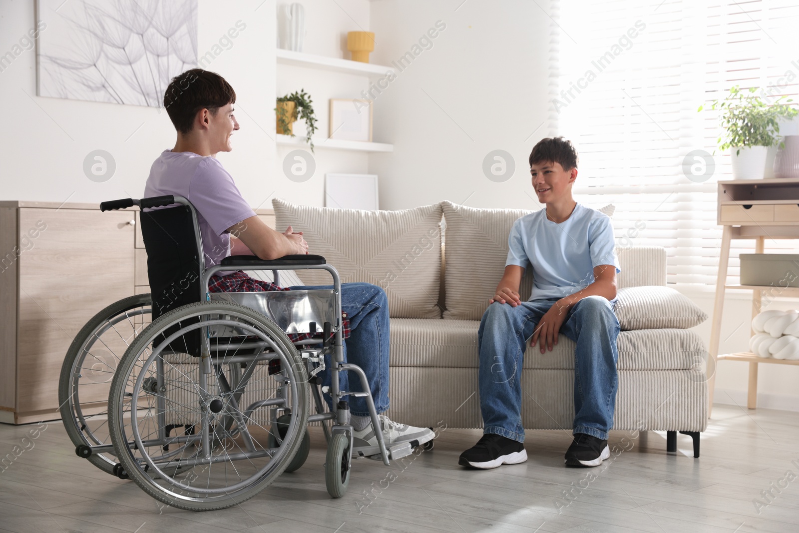 Photo of Happy young man in wheelchair and caregiver indoors