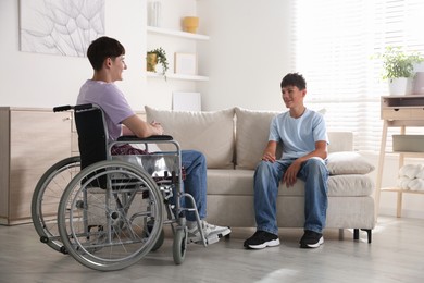Photo of Happy young man in wheelchair and caregiver indoors