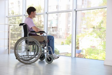 Photo of Young man in modern wheelchair indoors, space for text