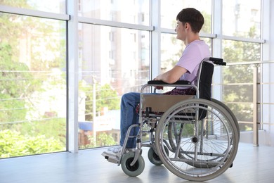 Photo of Young man in modern wheelchair indoors, space for text