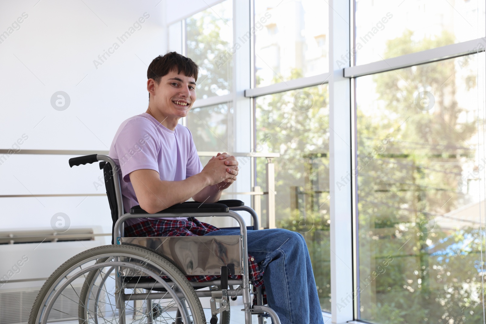 Photo of Happy young man in modern wheelchair indoors, space for text