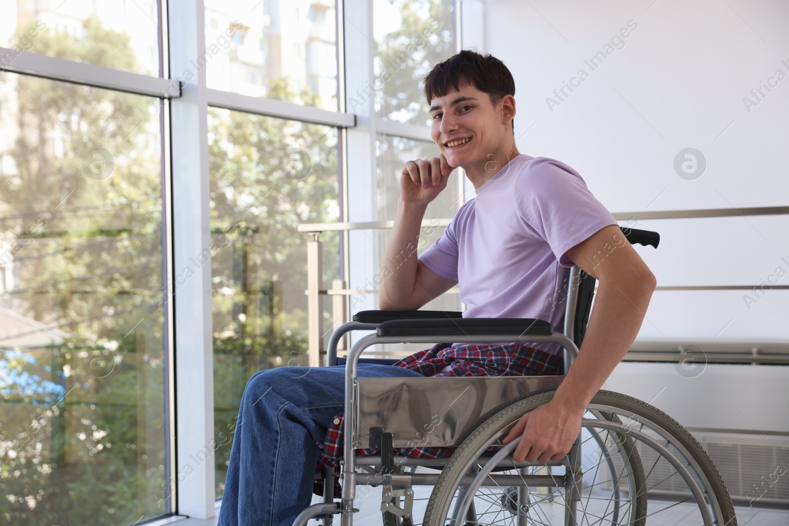 Photo of Happy young man in modern wheelchair indoors, space for text