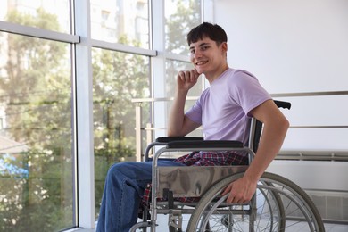 Photo of Happy young man in modern wheelchair indoors, space for text