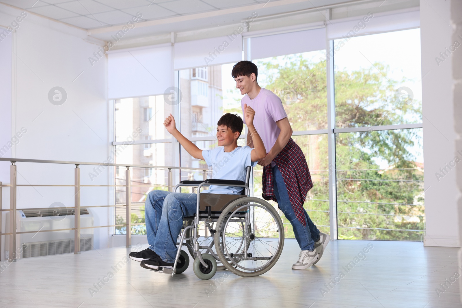 Photo of Happy teenage boy in wheelchair and caregiver indoors
