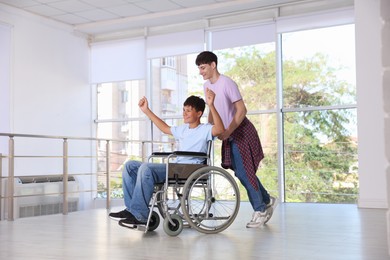 Photo of Happy teenage boy in wheelchair and caregiver indoors