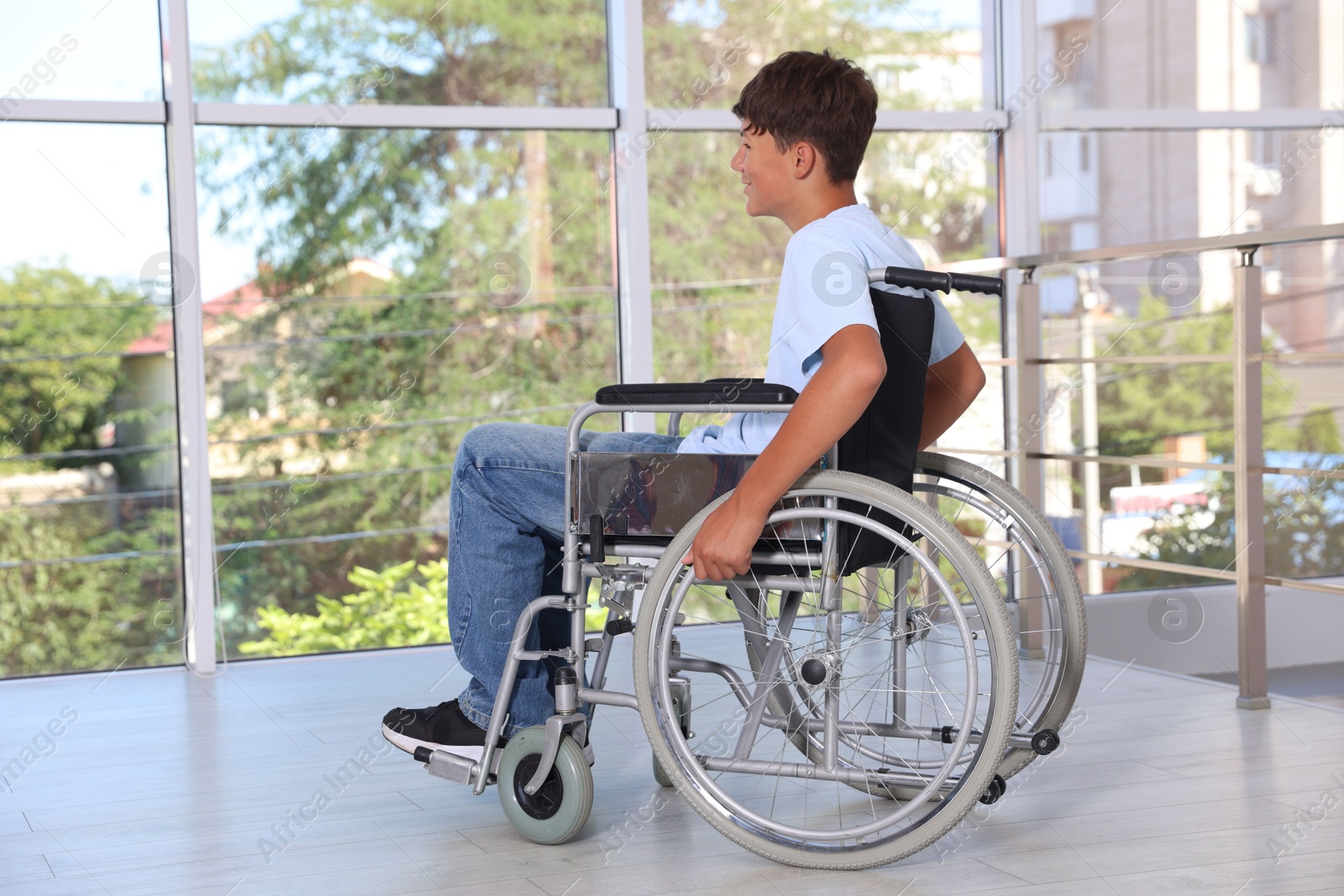 Photo of Teenage boy in modern wheelchair near window indoors