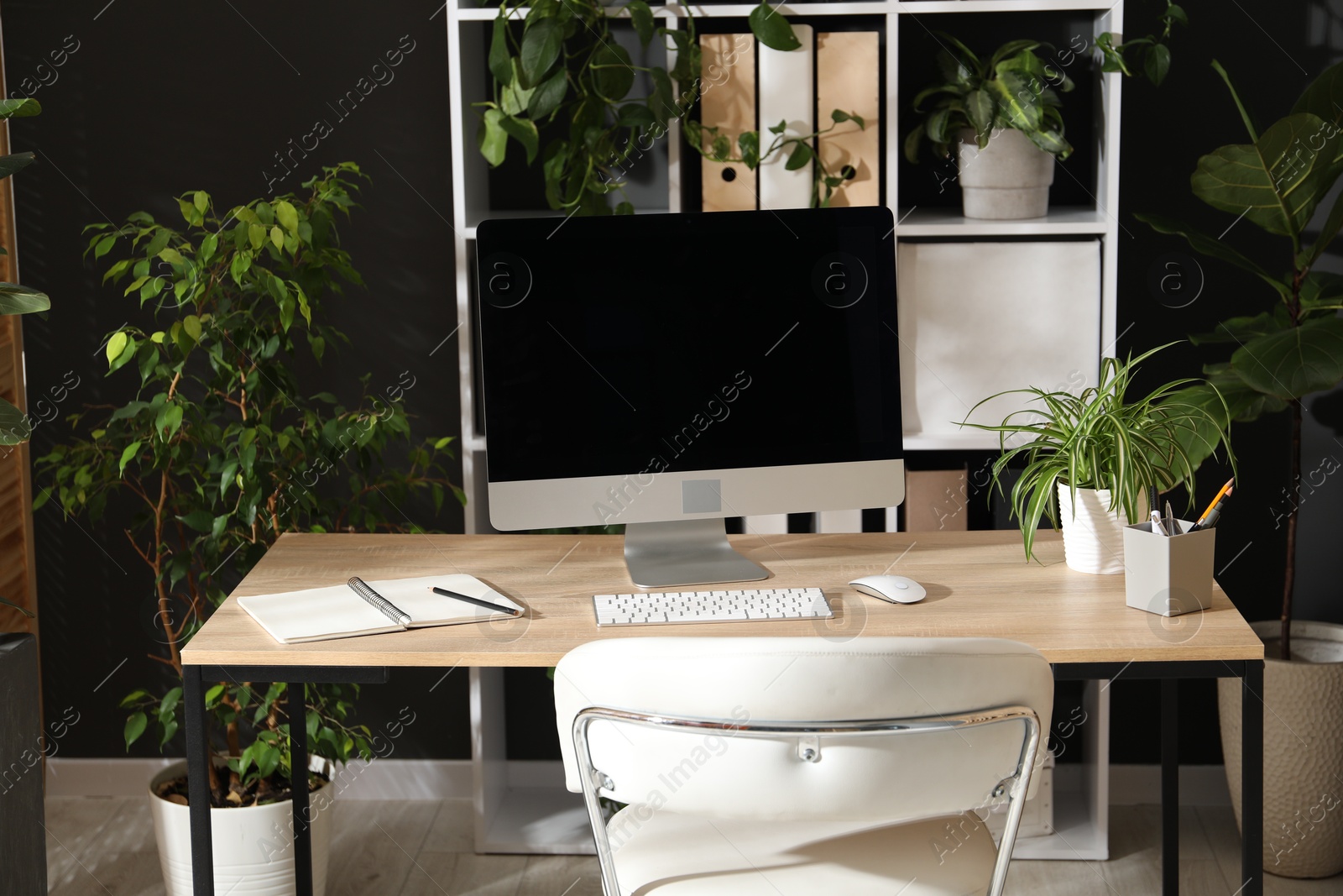 Stylish workplace with modern computer, stationery and floral decor in office. Biophilic interior design Photo of Stylish workplace with modern computer, stationery and floral decor in office. Biophilic interior design