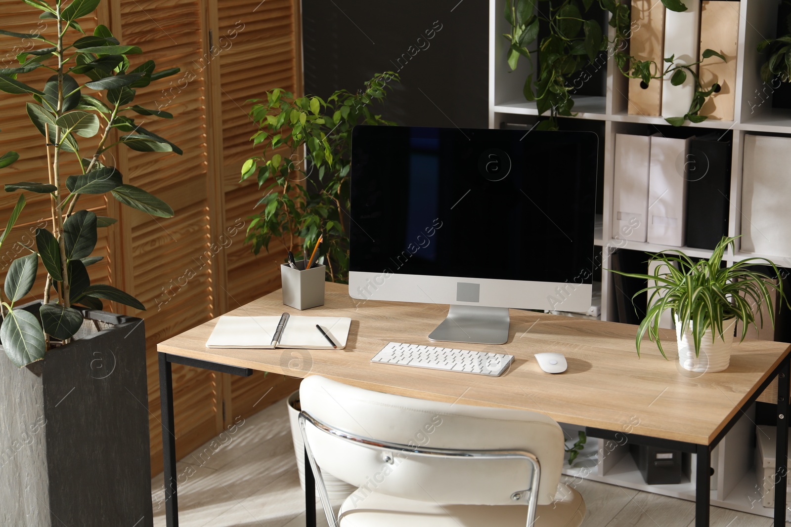 Stylish workplace with modern computer, stationery and floral decor in office. Biophilic interior design Photo of Stylish workplace with modern computer, stationery and floral decor in office. Biophilic interior design
