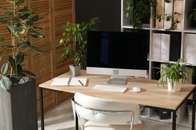 Photo of Stylish workplace with modern computer, stationery and floral decor in office. Biophilic interior design
