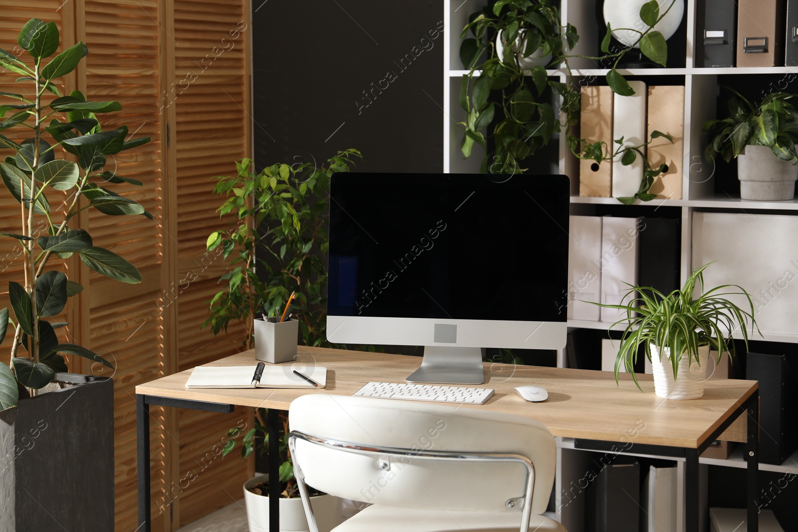 Stylish workplace with modern computer, stationery and floral decor in office. Biophilic interior design Photo of Stylish workplace with modern computer, stationery and floral decor in office. Biophilic interior design