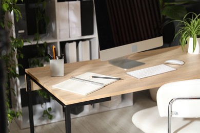 Photo of Stylish workplace with modern computer, stationery and floral decor in office. Biophilic interior design