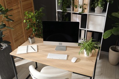 Photo of Stylish workplace with modern computer, stationery and floral decor in office, above view. Biophilic interior design