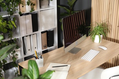 Photo of Stylish workplace with modern computer, stationery and floral decor in office. Biophilic interior design