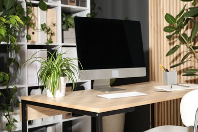 Photo of Stylish workplace with modern computer, stationery and floral decor in office. Biophilic interior design