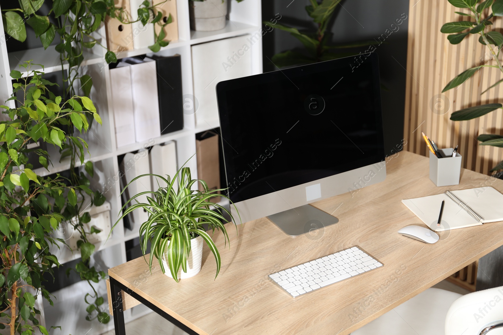 Stylish workplace with modern computer, stationery and floral decor in office. Biophilic interior design Photo of Stylish workplace with modern computer, stationery and floral decor in office. Biophilic interior design