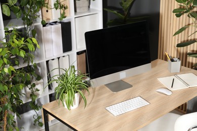 Photo of Stylish workplace with modern computer, stationery and floral decor in office. Biophilic interior design