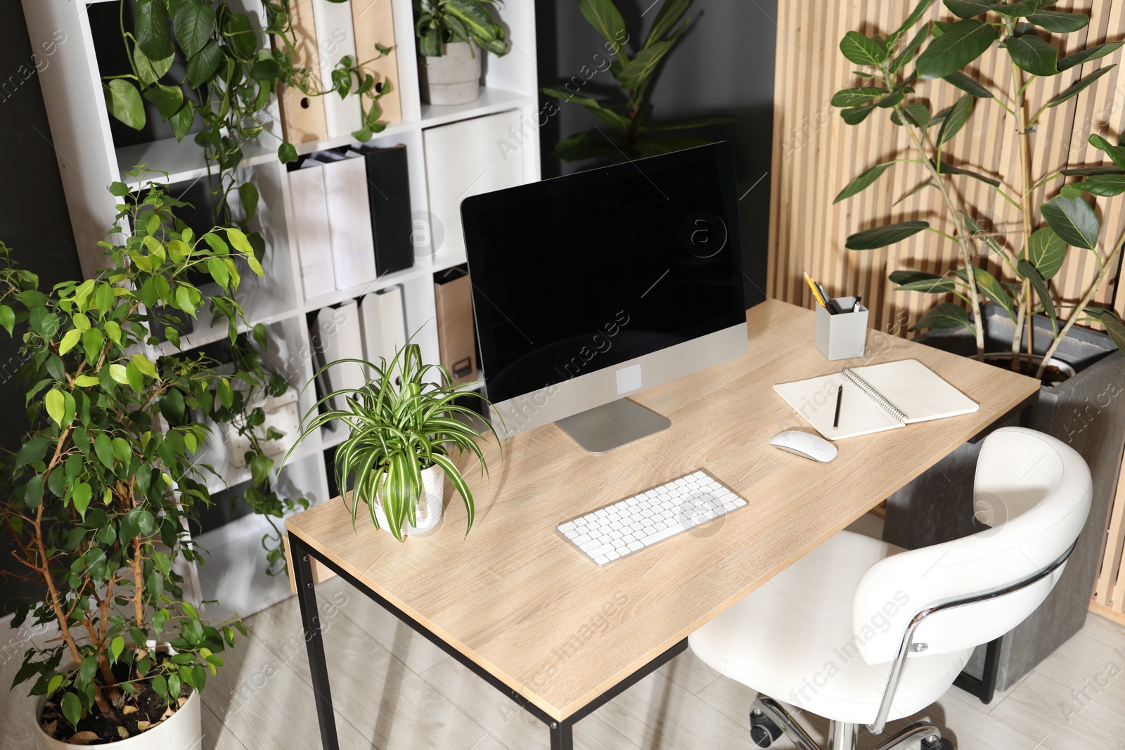Stylish workplace with modern computer, stationery and floral decor in office. Biophilic interior design Photo of Stylish workplace with modern computer, stationery and floral decor in office. Biophilic interior design
