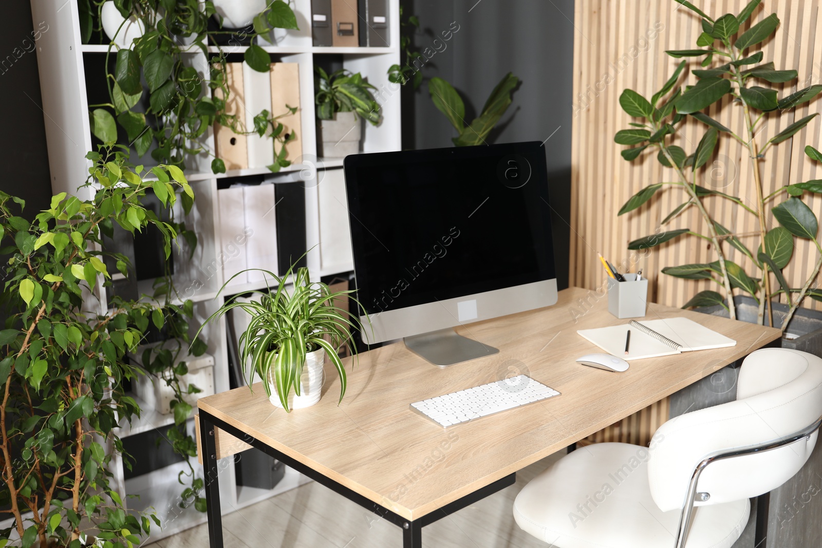 Stylish workplace with modern computer, stationery and floral decor in office. Biophilic interior design Photo of Stylish workplace with modern computer, stationery and floral decor in office. Biophilic interior design