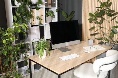 Photo of Stylish workplace with modern computer, stationery and floral decor in office. Biophilic interior design