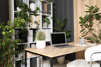 Photo of Stylish workplace with laptop, stationery and floral decor in office. Biophilic interior design