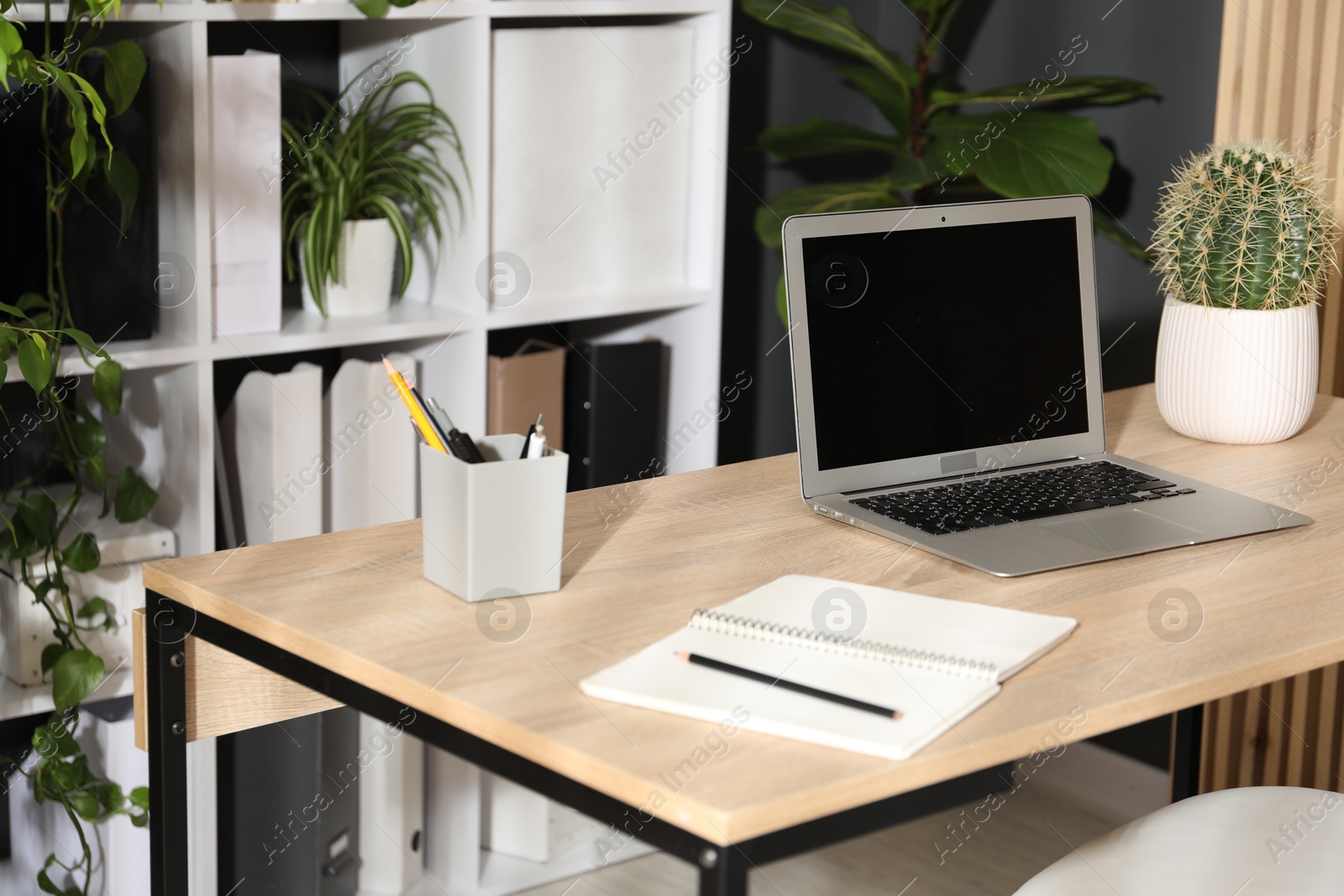 Stylish workplace with laptop, stationery and floral decor in office. Biophilic interior design Photo of Stylish workplace with laptop, stationery and floral decor in office. Biophilic interior design