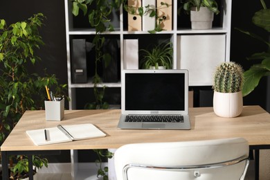 Photo of Stylish workplace with laptop, stationery and floral decor in office. Biophilic interior design