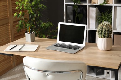 Photo of Stylish workplace with laptop, stationery and floral decor in office. Biophilic interior design