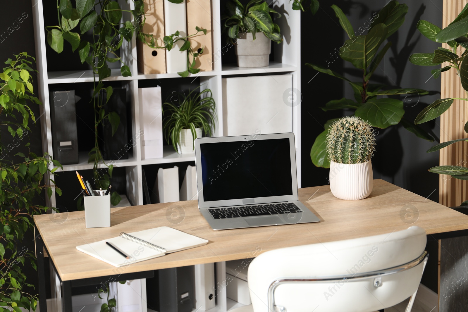 Photo of Stylish workplace with laptop, stationery and floral decor in office. Biophilic interior design