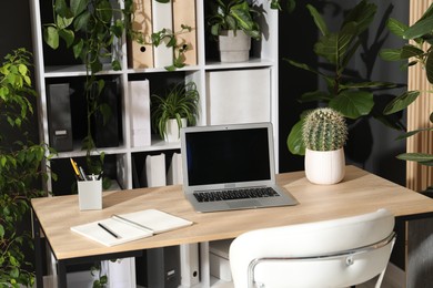 Photo of Stylish workplace with laptop, stationery and floral decor in office. Biophilic interior design