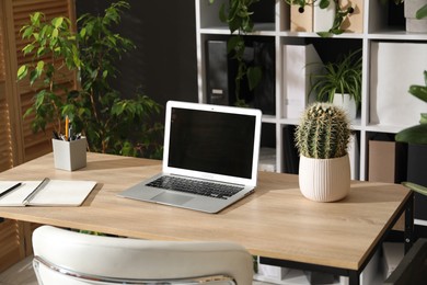 Photo of Stylish workplace with laptop, stationery and floral decor in office. Biophilic interior design