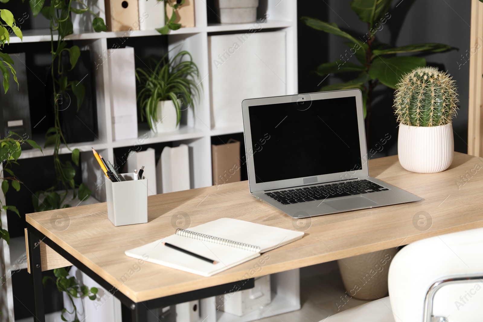 Photo of Stylish workplace with laptop, stationery and floral decor in office. Biophilic interior design